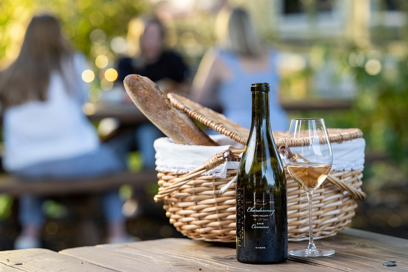 A bottle of Chardonnay with a glass and picnic basket in the background.