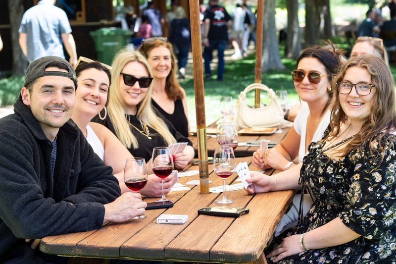 A group of friends at V. Sattui Winery enjoying wine and cards at an outdoor table.