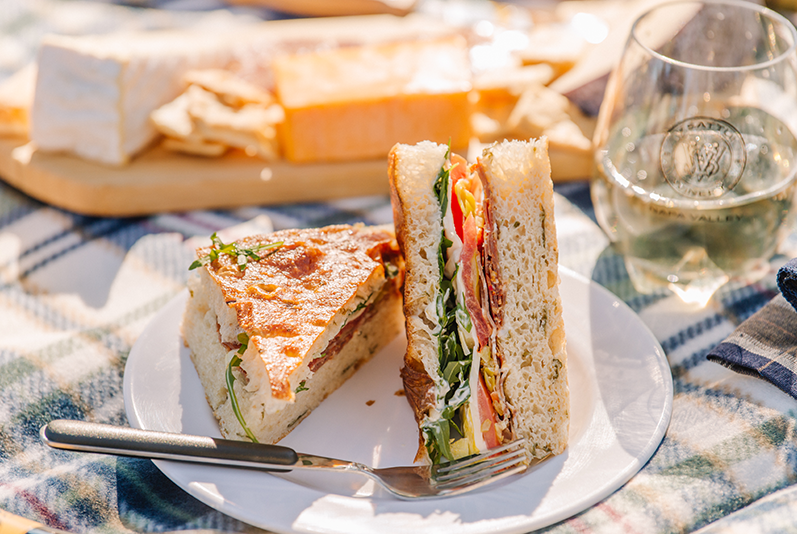 Picnic including V. Sattui's famous Italian Sandwich on foccacia, a variety of cheeses, and a glass of wine.