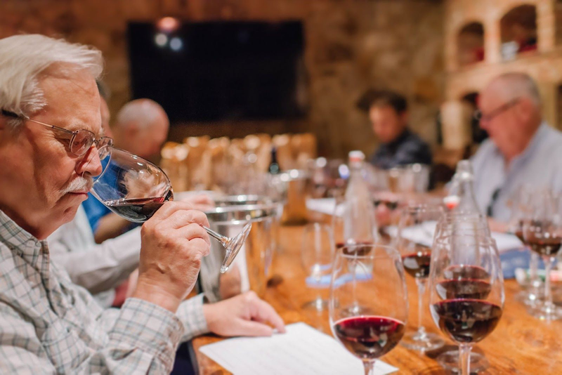 Elderly man at a wine tasting event smelling red wine in a glass.